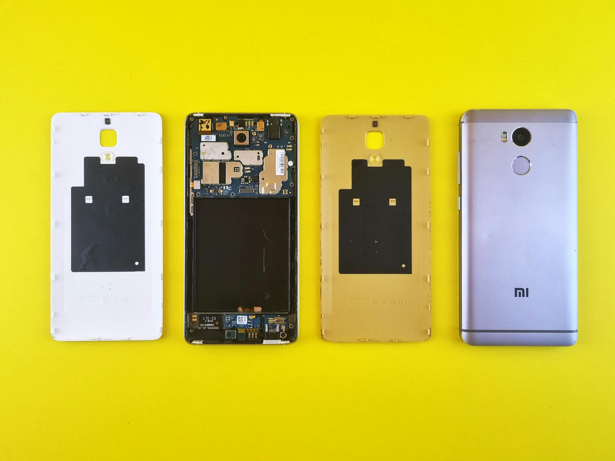 Close-up of disassembled smartphone on vibrant yellow surface, showing various parts.